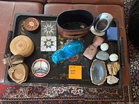 Photo of various coasters, decorative rocks, a blue hippo figurine, and a digital temperature and humidity gauge arranged on a decorated black tray on a couch.