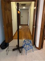 Wooden coat rack standing on carpet, tall with multiple hooks, black and blue metal shoe racks on floor nearby