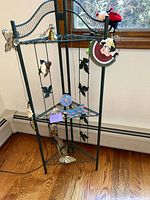 Photo showing green metal corner shelf with decorative trinkets, set near window and wooden floor.