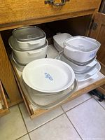 Photo showing stacked white CorningWare baking dishes with lids in a wooden drawer.