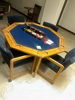 View of octagonal wooden framed game table with blue felt top and built-in chip tray, surrounded by four padded chairs.