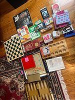 Wide view of assorted board games and puzzles laid out on floor including Scrabble, dominoes, cards, backgammon, and Spirograph.