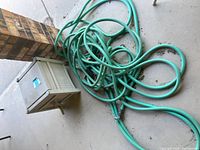 Coiled green garden hose loosely placed on concrete floor near brick pillar.