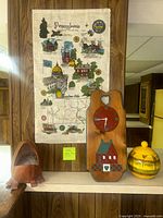 Photo showing the Pennsylvania state map hanging, wooden heart-shaped cutout clock, and yellow striped ceramic jar on a shelf against wood paneling.