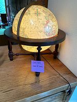 Front and side views of the illuminated globe on a dark wooden circular stand showing continents and oceans.