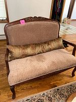 Front-facing view of one of the loveseats showing fabric upholstery, carved wood frame, and decorative cushion.