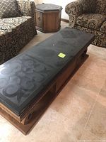 Photo of the dark Mediterranean style coffee table with patterned top and hexagonal end table situated in a living room between two upholstered seats.