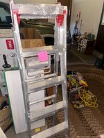 Full view of the metal ladder folded, showing red top frame and five wide steps.