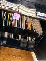 Photo of two shelves filled with various spiral bound and loose sheet music booklets and books, mostly piano music.