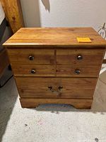 Front view of wooden nightstand showing three drawers with round knobs and a metal handle on the bottom drawer; visible scratches and wear marks on wood surface.