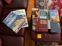 Photo showing 11 assorted non-fiction books including atlases, thesaurus, medical terms book, a biography, and more arranged on a dark sofa.