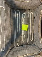 Top-down view of nine pearl necklaces arranged on a soft fabric surface in a jewelry display; necklaces vary in pearl size and color.