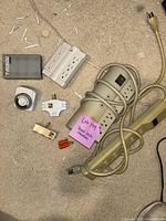 Lot contents showing assorted power cords, adapters, extension cords, and timer switch arranged on floor.