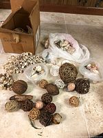 Wide view of the lot showing cardboard box labeled 'seashells', several plastic bags with mixed seashells, and multiple decorative woven spheres in natural shades scattered on the floor.