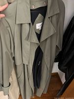 Photo of khaki trench coat hanging on a rack showing front collar and button details.