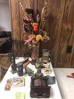 Full view of small decor items including dried flower arrangement, statuettes, coasters, and colorful glass vase on a surface in front of wood paneling