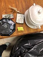 White ceramic soup tureen with lid, bird sculpture, box of cheese markers, fish figurines on black enameled tray