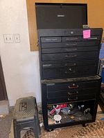 Full view of large black metal Storehouse tool box with drawers and black plastic step stool on floor next to it