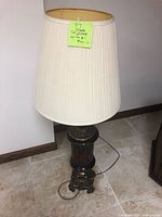 Full view of the tall lamp showing cream-colored pleated lampshade and ornate base in red, black and brass colors.