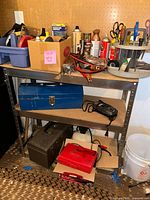 Metal shelving unit with various tools, tool boxes, and cans of spray paint arranged on three shelves.