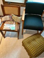 Two chairs, one with cane backrest and floral cushion with decor pillows, the other chair is upholstered in blue fabric, with a plaid ottoman visible.