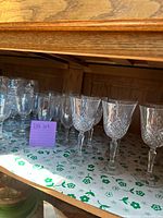 Glassware set with crystal-cut pattern wine glasses and other clear glass glasses viewed from side angle on shelf.