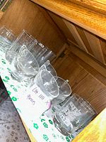 Various clear glass cups and bowls arranged on a green and white floral cloth inside a wooden cabinet.