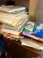 Stack of assorted papers, folders, and office supplies on a wooden surface.