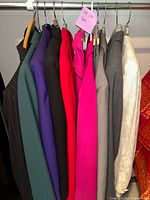 Photo of various women's suit jackets hanging on a rack, showing multiple colors and textures including green, purple, black, red, pink, gray pinstripe, and cream.