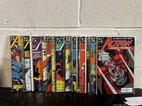 Photo of 16 comic books in lot, issues #605 through #620 of Action Comics, standing upright against a white wall. Covers visible showing vibrant artwork.