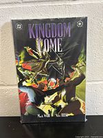 Front cover of Kingdom Come graphic novel showing colorful superhero characters and title.