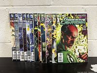 Front view of twelve Green Lantern comic books from the 2011 series, issues #1 through #12, arranged side by side showing their front covers.