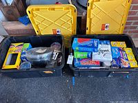 Two large black bins with yellow lids containing assorted disposable entertaining supplies