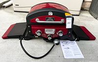 Front view of Smoke Hollow red tabletop propane grill with side shelves, regulator hose and manual visible