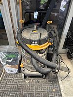 Front view of Vacmaster Professional Beast stainless shop vac with hose, cord and accessory bag beside
