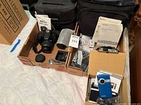 Overview of both boxes showing Canon DSLR with lens, extra lens, two camera bags, Sony camcorder, blue Sylvania camcorder, accessories
