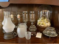 Group shot of entire lot on shelf showing hurricane lamps, spare shades, votive holders, Kerr jar candlesticks, potpourri dishes and trinket dish