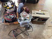 Overall lot showing Stanley jump starter, Sears charger box, Optima charger, clamp meter, clear bin with cables