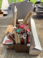 Overview of cardboard box containing numerous wrapping paper rolls, inflatable bear box partially visible, and white box