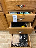 Open cabinet with three drawers showing colorful knives in upper drawer, nylon utensils, gloves