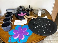 All items displayed on table including GreenPan skillets, Cook's Essentials pots, pizza pans, aluminum pans with lids, silicone strainer, flower mats