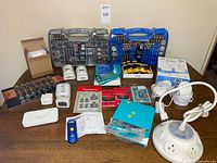 Overview of entire lot on tabletop showing monitor, toolkits, batteries, flashlights, IR thermometer and accessories