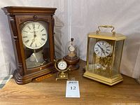 Front view of all four timepieces: Howard Miller mantle clock, Bulova brass mantle clock, Keystone pocket watch under dome, Hamilton pocket watch in holder
