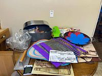 Group shot of all kitchen items on table including roaster, skillet, mats, racks, press, timer