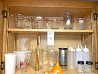 Overall lot on two shelves showing measuring cups upper, storage and condiment items lower