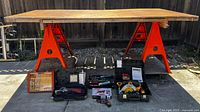 Overall lot showing plywood surface on two orange sawhorses with power tools and accessories laid out