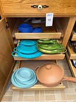 Drawer view showing stacked blue baking dishes, collapsed blue colanders, green bowls, light blue discs and copper-tone skillet