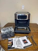 Air fryer oven with door open, mesh basket, manuals and accessories visible