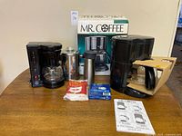 Full lot showing three coffee makers, stainless percolator, travel mug, two filter packs and Mr. Coffee box