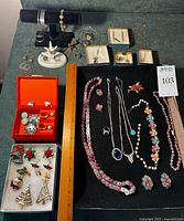 Overall lot view with jewelry arranged on black board, bracelets on stand, ring holder, boxes and two trays